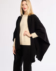 Woman wearing a black poncho over a beige sweater on a white background