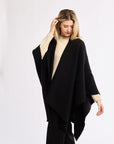 Woman wearing a black poncho over a beige top on a white background