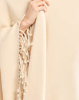 Beige scarf with fringe held by a hand against a beige background