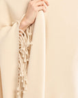 Beige scarf with fringe held by a hand against a beige background