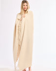 Woman wearing a beige poncho with fringe details on a white background