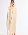 Woman wearing a beige poncho with fringe details on a white background