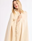 Woman wearing a beige blanket with tassels on a white background