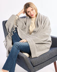 Woman sitting on a chair wearing a gray blanket draped over her shoulders against a white background