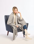 Woman sitting in a chair wearing a gray blanket draped over her shoulders on a white background