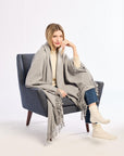 Woman sitting in a chair wearing a gray blanket draped over her shoulders on a white background