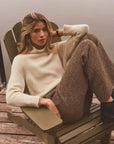 Woman modeling tweed pants and a cashmere sweater in a chair outside