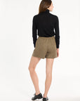 A woman modeling the Painter's Fleck Herringbone Archer Shorts with a black turtleneck and loafers, back view, photographed against a plain white studio background.