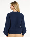 A woman modeling the navy Baby Cashmere Ribbed Crewneck with camel trousers, back view, photographed against a plain white studio background.