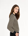 A woman modeling the Black Tri-Color Check Classic Cashmere Crew with black trousers, side view with one hand in a pocket, photographed against a plain white studio background.