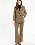 A woman modeling the double-breasted Painter's Fleck Herringbone Cynthia Blazer with a black turtleneck and matching trousers, front view, photographed against a plain white studio background.