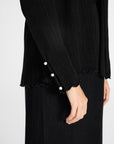 Close up of pleated black cardigan with gemstones buttons on the sleeve on a white backdrop