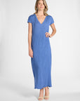 A woman modeling a blue pleated silk dress with nude heels on a white background
