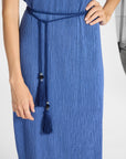 A close-up of a model wearing a blue textured midi dress with a matching braided belt featuring dark buttons and tassels.
