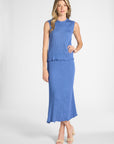 Woman modeling a pleated silk shell with the matching blue skirt on a white backdrop