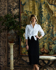 Woman standing in front of rugs wearing a black pleated skirt and a white button down blouse