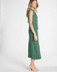 A woman modeling a sleeveless green blouse and skirt with a textured crinkle fabric and ruffled trim, shown in profile against a light gray studio background.
