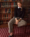 Woman sitting on a chair in front of a bookshelf wearing a black cable knit sweater with tweed pants
