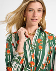 Woman wearing a patterned long sleeve dress with green, orange, and white design on a plain background