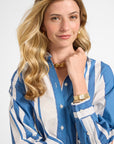 Woman wearing a blue and white striped shirt with gold jewelry jewelry on a plain background