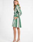 Woman modeling a white and green striped dress with white heels on a plain backdrop