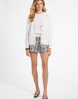 Woman wearing a white cardigan, patterned shorts, and black shoes on a white background