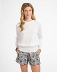 Woman wearing a white crewneck and patterned shorts on a white background
