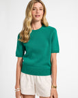 Woman wearing a green sweater and white shorts on a white background
