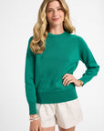 Woman wearing a green crewneck and white shorts on a white background