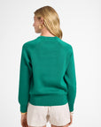 Woman wearing a green crewneck and white shorts on a white backdrop