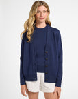 Woman wearing a blue cardigan over a white top and shorts on a white background