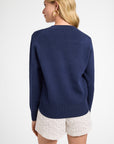 Woman wearing a long sleeve blue sweater and white shorts on a plain background
