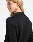 Woman wearing a black cardigan and gold jewelry with a plain background
