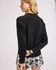 Woman wearing a black crewneck and floral shorts on a plain background