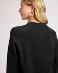 Woman wearing a black long sleeve sweater with a plain background