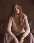Woman modeling a tan cashmere turtleneck sweater while sitting on a couch