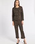 A woman modeling a matching brown tweed jacket and cropped trousers set with gold-tone buttons, paired with black pointed-toe heels, against a plain light gray studio background.