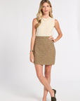 A woman modeling a sleeveless cream cable-knit top paired with a brown and beige plaid mini skirt, styled with dark olive loafers against a light gray studio background.