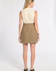 A woman shown from the back wearing a cream cable-knit sleeveless top and a brown and beige plaid mini skirt, paired with dark brown shoes, against a plain white studio background.