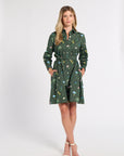 A woman modeling a dark green long-sleeve shirt dress with a colorful floral print, standing against a plain white studio background.