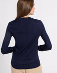 A woman shown from the back wearing a navy blue long-sleeve knit top and beige pants against a plain light gray studio background.