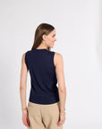A woman shown from the back wearing a sleeveless navy top and beige pants, standing against a plain light gray studio background.