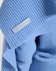 Close up image of a blue cashmere sweater with a leather label that says Eleanor Leftwich