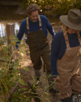 Couple wearing outdoor gear, including the Men's Redford Crew sweater in navy, walking through a forest near a stream during a nature activity.