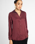 A woman wearing a long-sleeve button-up blouse with vertical stripes in a deep burgundy and maroon color, paired with black pants, against a plain light gray background.