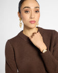 Close view: woman wearing a classic crewneck sweater in Chocolate brown with black pants in front of a white background