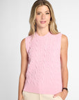A woman modeling a sleeveless light pink cable-knit sweater vest against a light gray studio background.