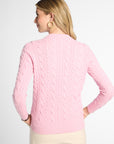 A woman shown from the back wearing a light pink cable-knit sweater and cream pants against a plain light gray studio background.