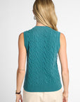 A woman shown from the back wearing a sleeveless teal cable-knit sweater vest over a light beige top and pants, against a plain light gray studio background.