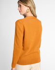 A woman shown from the back wearing a solid orange knit sweater and cream-colored pants, photographed against a clean white studio background.